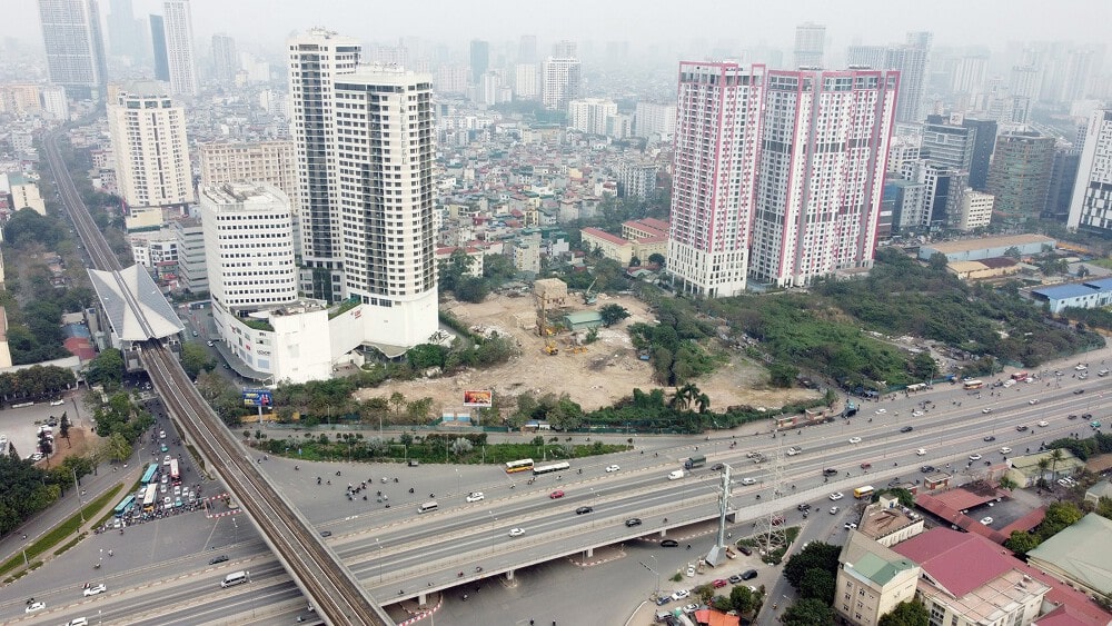 Sun Xuân Thủy Cầu Giấy 21 Hình ảnh từ trên cao thể hiện tiến độ xây dựng dự án Sun Xuân Thủy - Cầu Giấy, với khu đất trống, máy móc và vật liệu xây dựng bao quanh bởi các tòa nhà cao tầng, đường cao tốc và cầu vượt nhộn nhịp.
